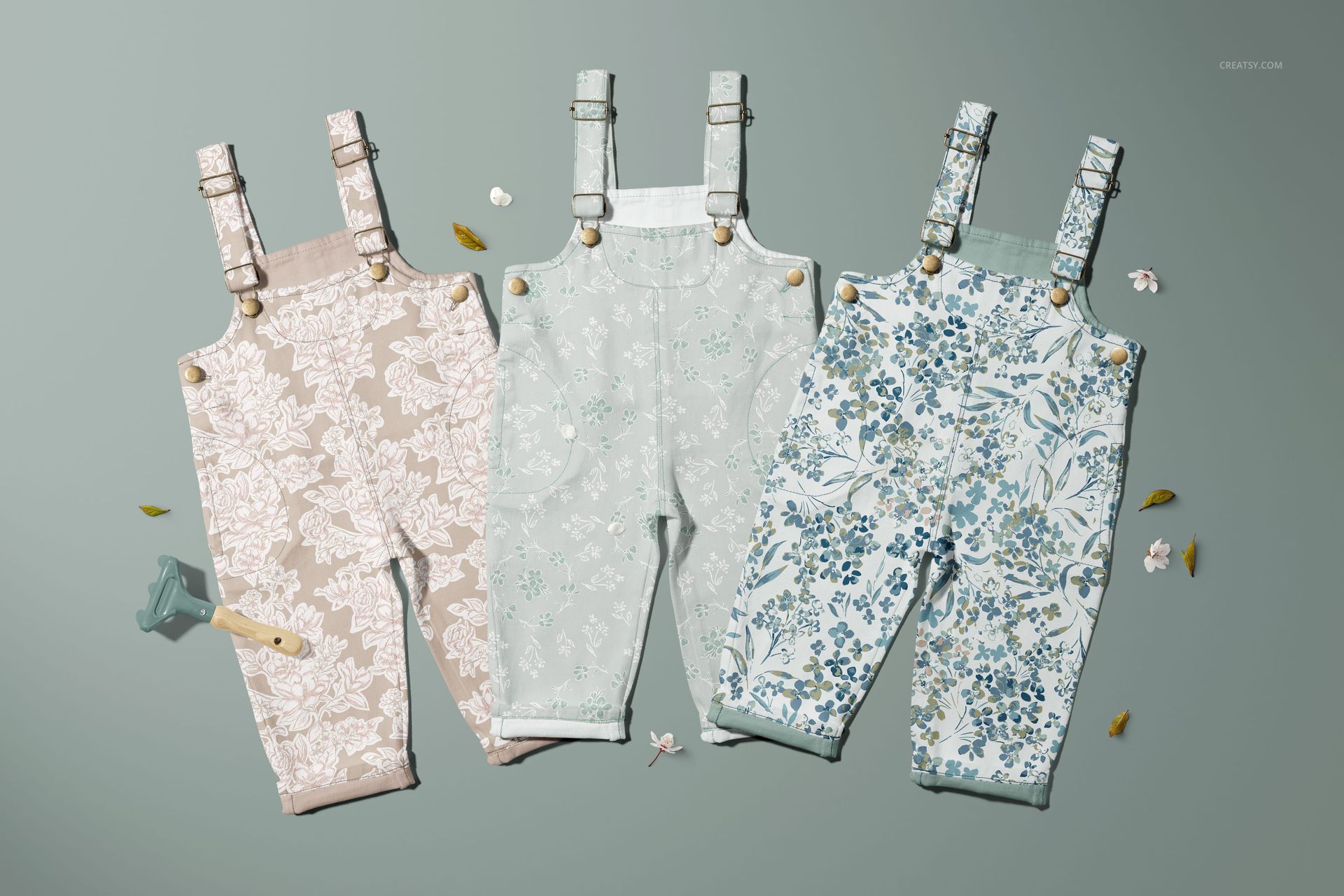 PSD mockup of three floral-patterned dungarees for children, displayed on a light background with scattered leaves and petals.