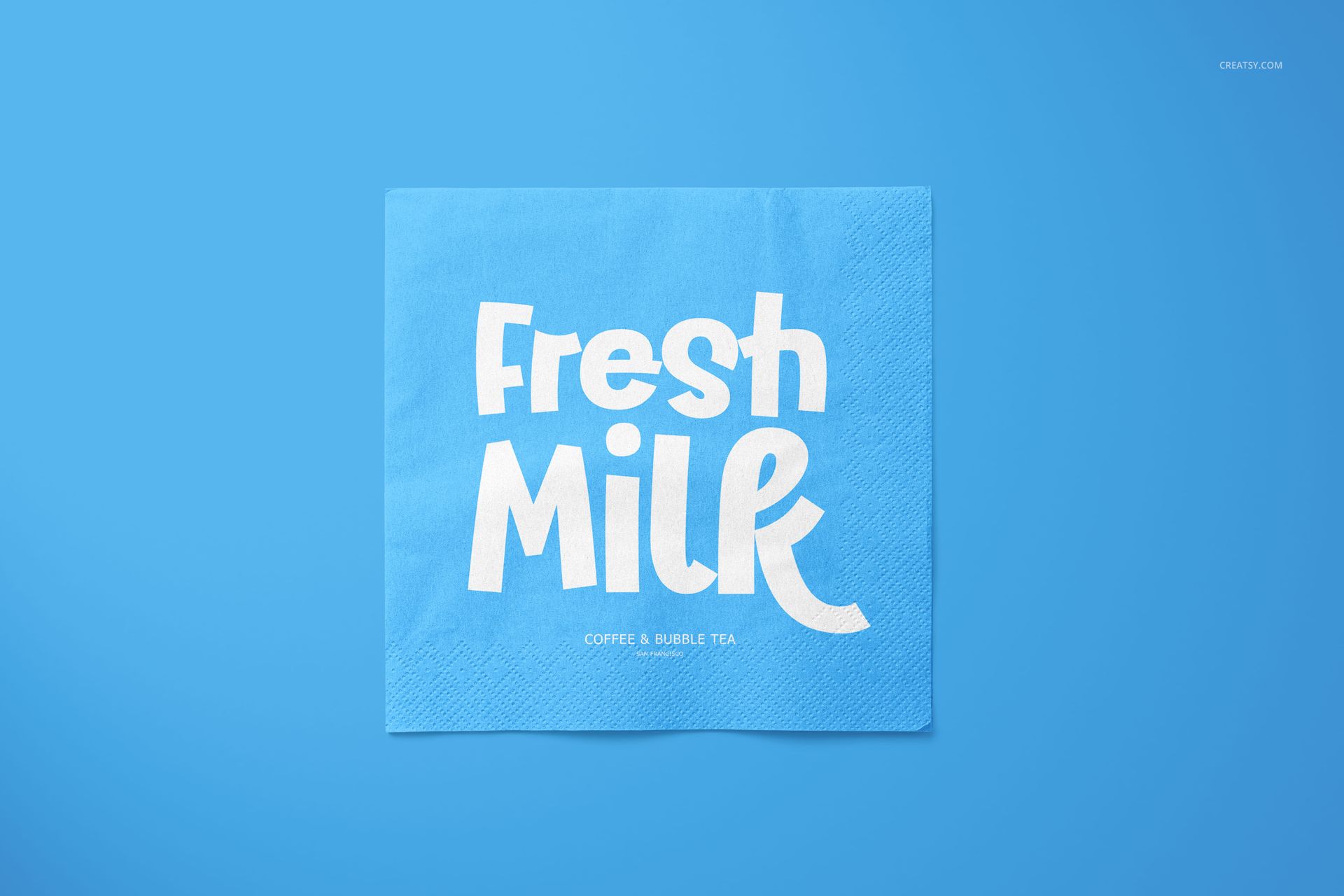 Square napkin mockup featuring a bold white 'Fresh Milk' print on a blue background, shown from a top view.