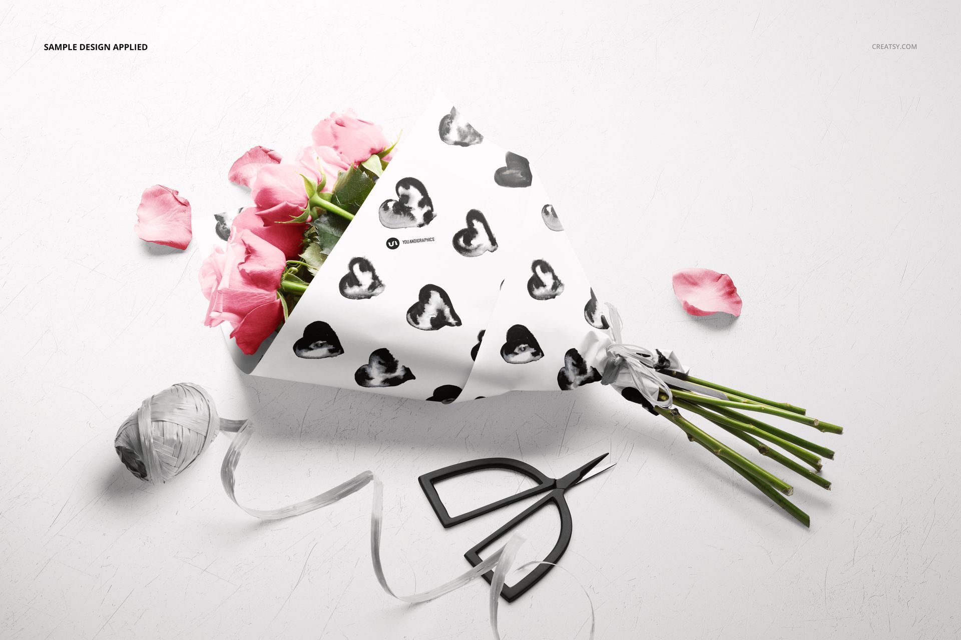 PSD mockup featuring pink roses wrapped in white paper with black hearts, displayed on a light background with ribbon and scissors.