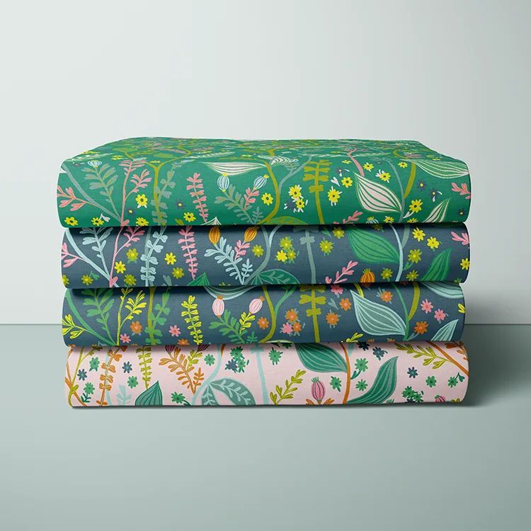 Folded fabrics mockup showing four stacked pieces with botanical patterns in green, blue, yellow, and pink tones.