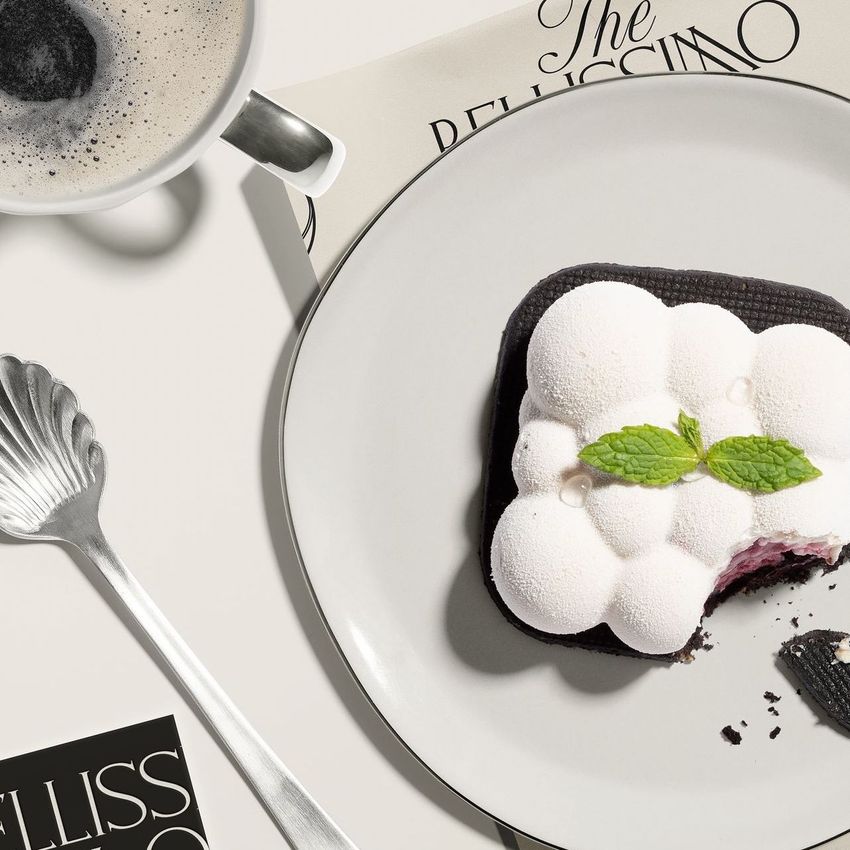 Food safe paper mockup featuring a white dessert with mint leaves on a plate, beside a cup of coffee and printed paper.