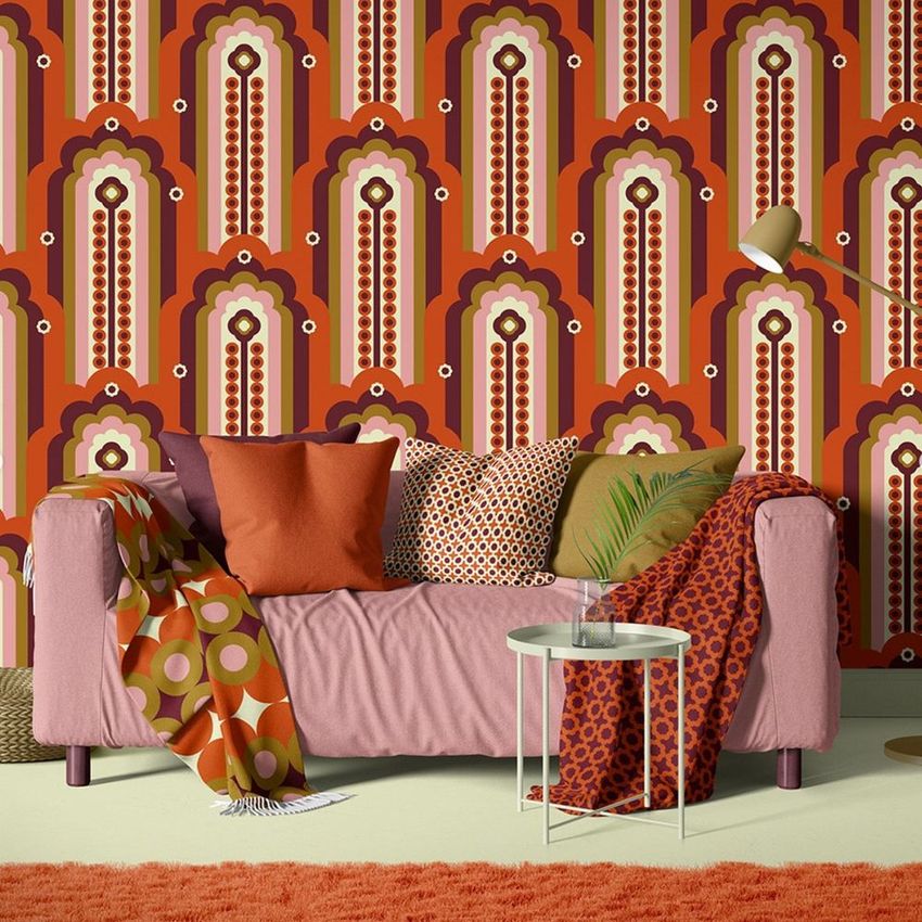 Modern living room wallpaper mockup featuring a pink sofa with assorted patterned pillows and a retro geometric wall design.