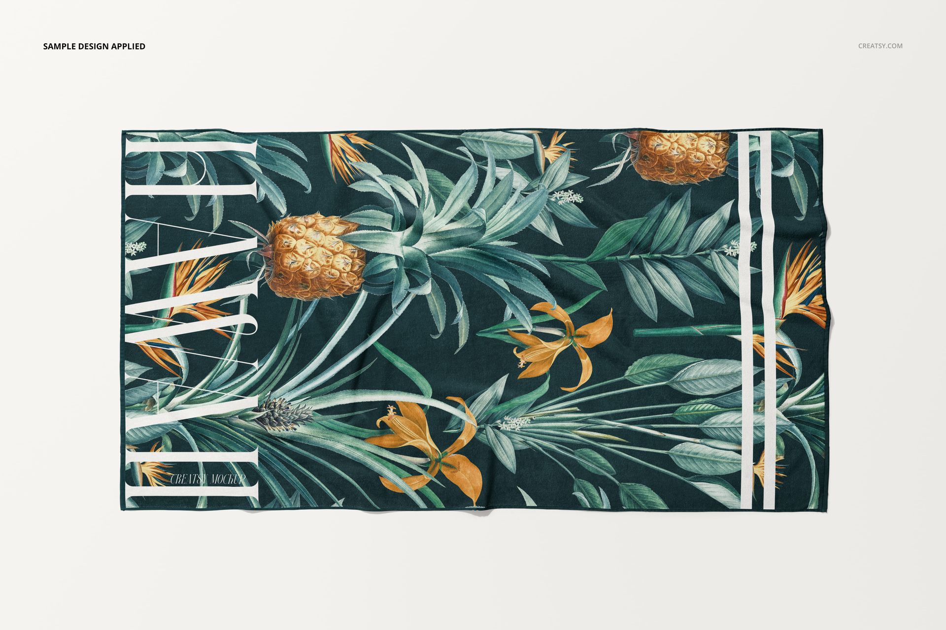 Top view of a beach towel mockup featuring green foliage, pineapples, and orange flowers on a dark background.