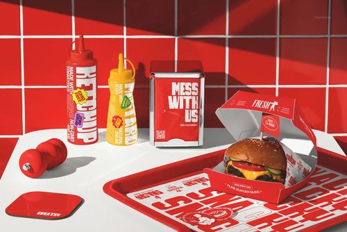 Fast food restaurant branding mockup featuring a burger in an open box, condiment bottles, and a branded tray on a white table.