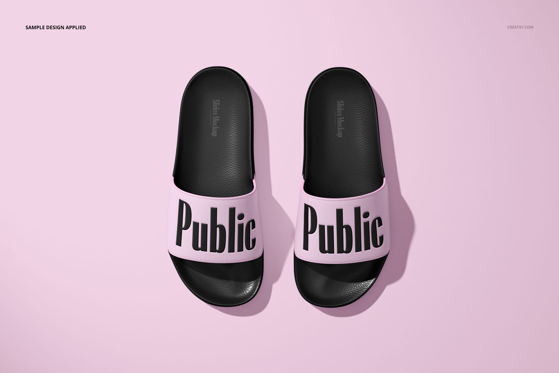 PSD mockup of two black slide sandals with light pink bands and prominent black text, displayed on a pink backdrop.