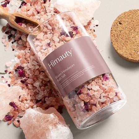 Bath salt label mockup showing a clear jar filled with pink Himalayan salt and dried petals, featuring a mauve label on a beige surface.