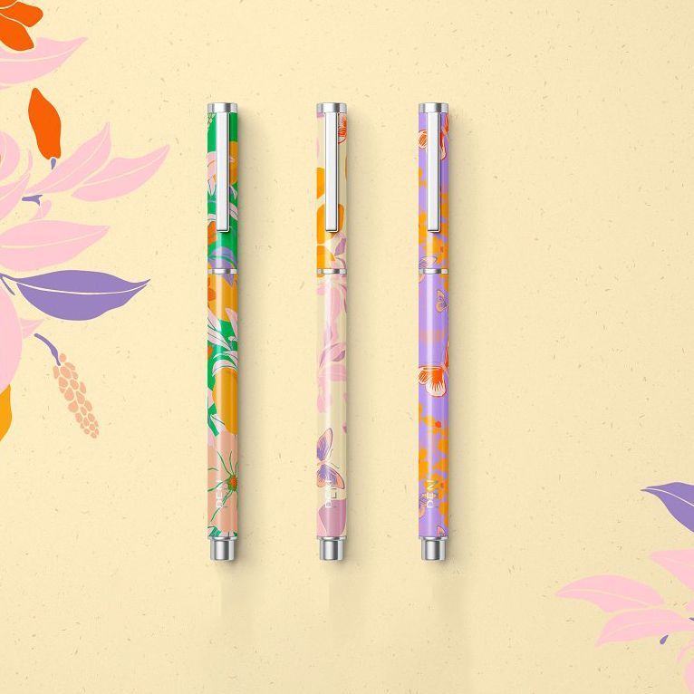 Stationery set mockup featuring three decorative pens with colorful floral patterns on a light beige background with leaf illustrations.