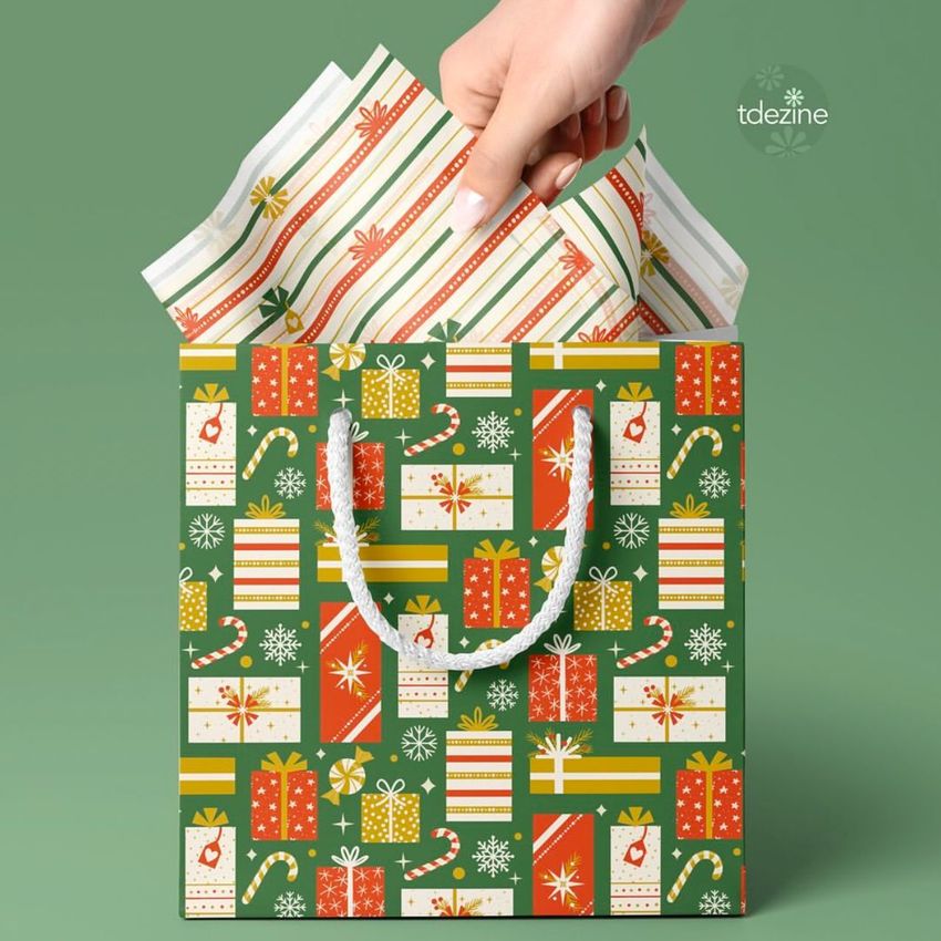 Hand placing striped tissue paper into a festive gift bag mockup with holiday patterns, set against a green background.