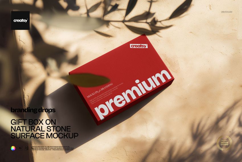 Red rectangular packaging box mockup on a beige stone background, viewed from above with leafy shadows across the scene.