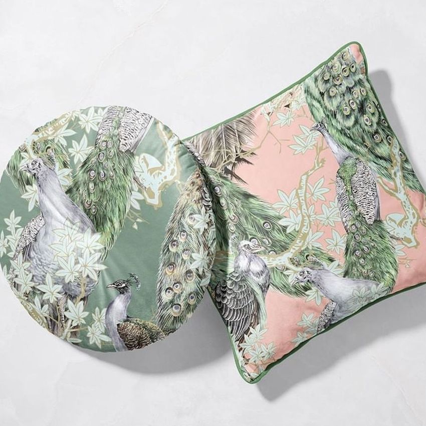 Square and round velvet cushion mockup with piping, featuring peacock and leaf illustrations on pastel backgrounds, placed on a light surface.