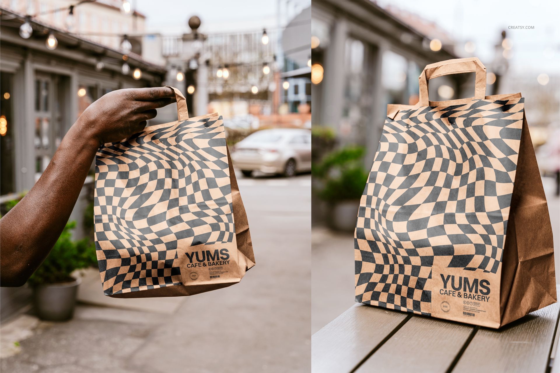 Paper bag mockup featuring a bold black checkered design, displayed outside with urban scenery and hand holding the bag.
