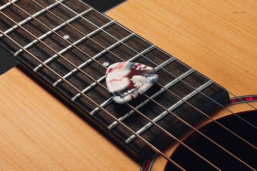 Guitar pick featuring abstract swirls placed across the fretboard of a wooden acoustic guitar in a PSD mockup scene.
