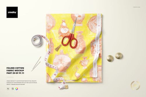 Top view of folded cotton fabric mockup featuring a decorative vase print, scissors, tape measure, and coins on a light surface.