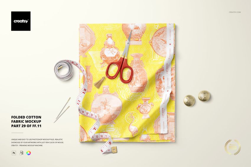 Top view of folded cotton fabric mockup featuring a decorative vase print, scissors, tape measure, and coins on a light surface.