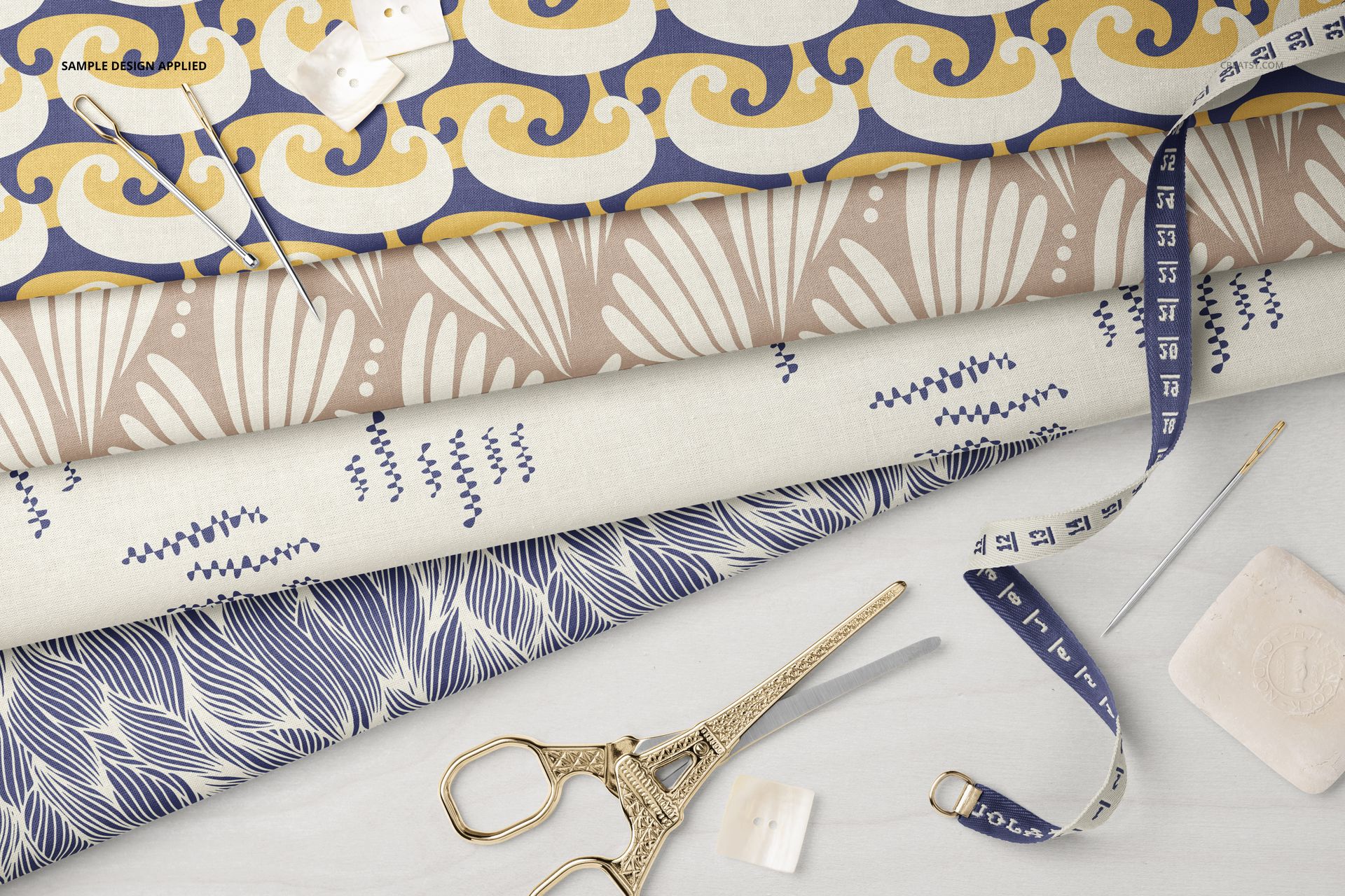 Four folded cotton fabrics with different designs, displayed with tailor tools on a light surface in a PSD mockup.