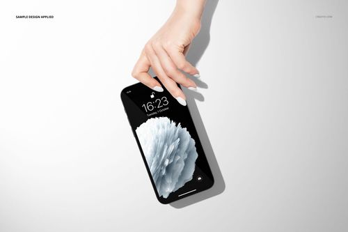 PSD mockup featuring a hand gripping a black iPhone 12, screen showing a grayscale floral pattern on white backdrop.