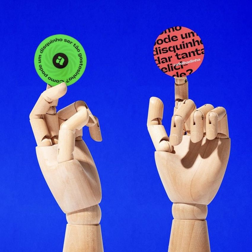 Two wooden mannequin hands hold round sticker mockups against a solid blue background, each featuring bold patterns and text.