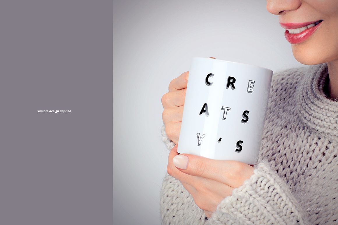 Front view of a woman holding a white ceramic mug with bold black text, wearing a light knitted sweater.