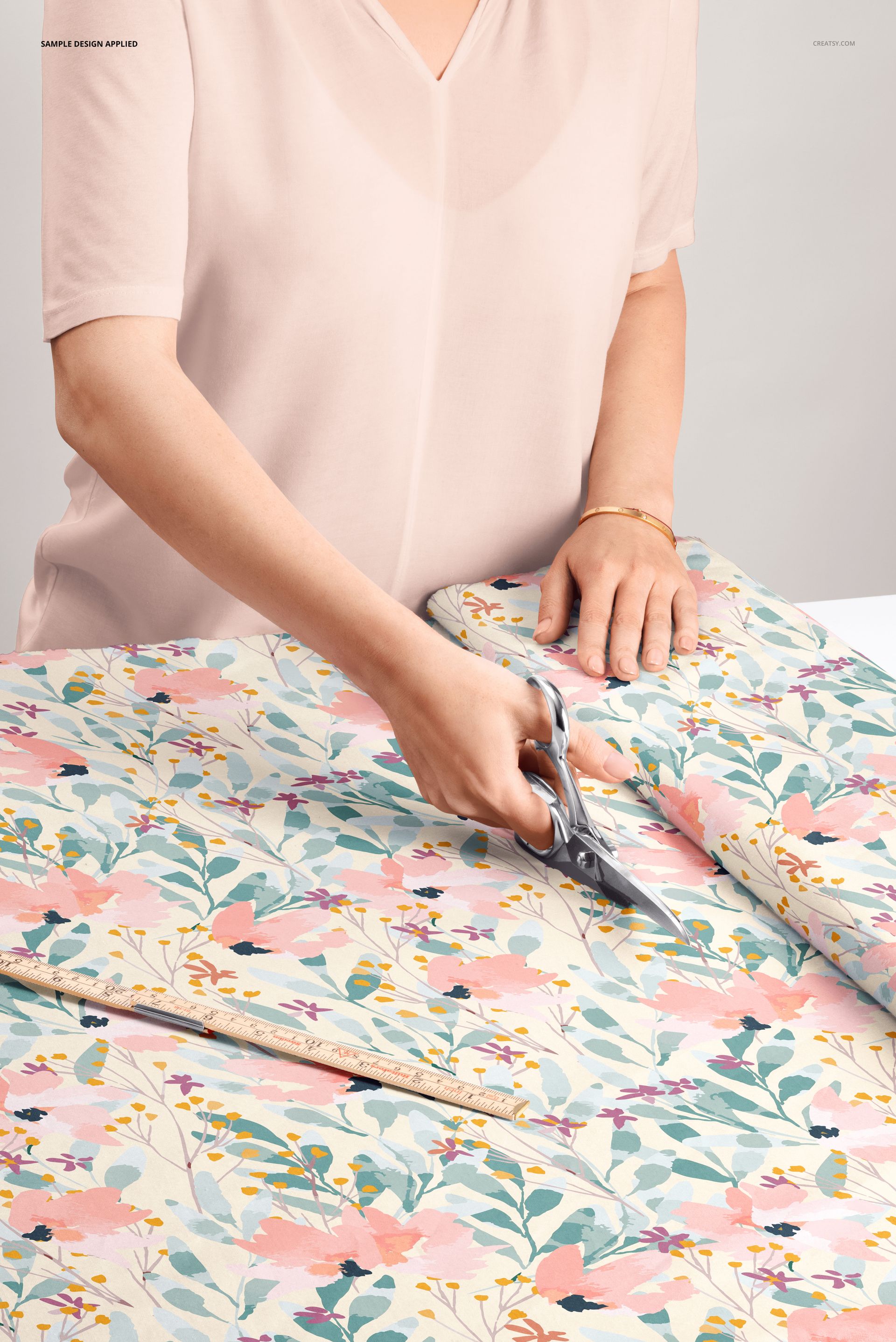 PSD mockup of a person trimming colorful botanical fabric on a table, floral design in soft pastel tones.