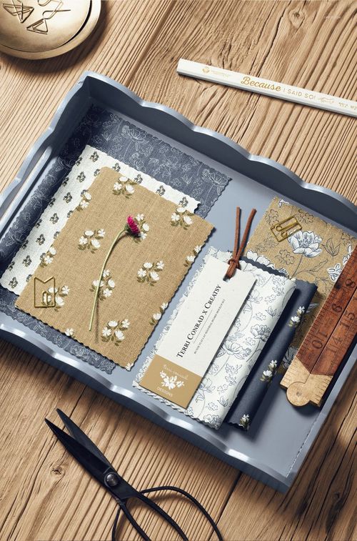 Flat lay of a moodboard mockup featuring floral and patterned fabric samples, stationery, and crafting tools on wood.