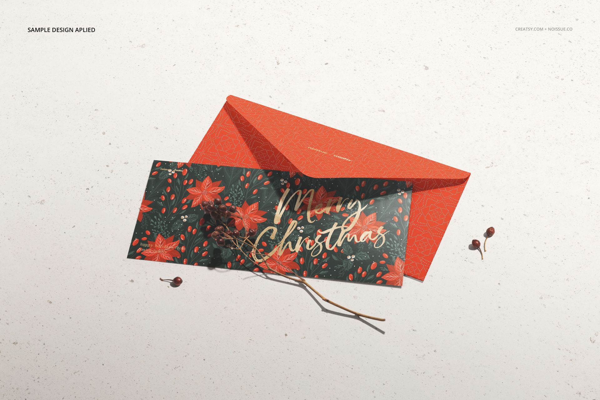 Front view of a stationery mockup featuring a festive card and orange envelope, with botanical props beside them.