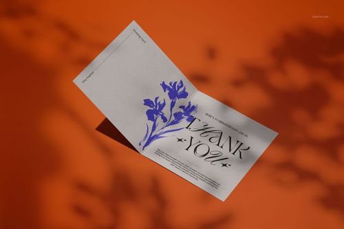 Square greeting card mockup with a gray card featuring blue floral artwork and elegant text, shown on an orange surface.