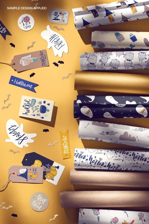 PSD mockup featuring Halloween wrapping paper rolls, decorative tags, and stickers on a yellow tabletop.