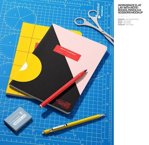 Stationery mockup with notebooks, pencils, scissors, and sharpener displayed on a blue grid cutting mat from above.