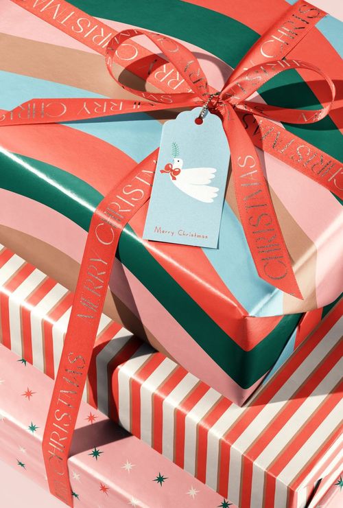 Stacked Christmas gift boxes wrapped in colorful striped and star-patterned paper with red ribbon and festive tag.