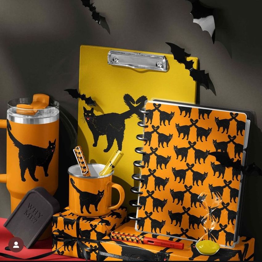 Halloween desk stationery and drinkware mockup featuring black cat and bat motifs on orange and yellow items, arranged on a dark surface.