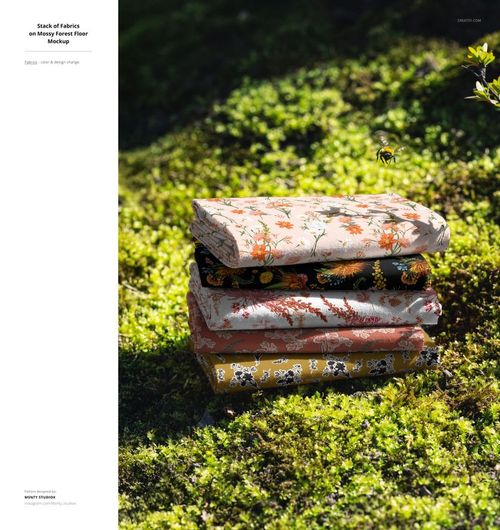 PSD mockup featuring a stack of colorful fabric pieces with nature-inspired prints placed on a forest ground.