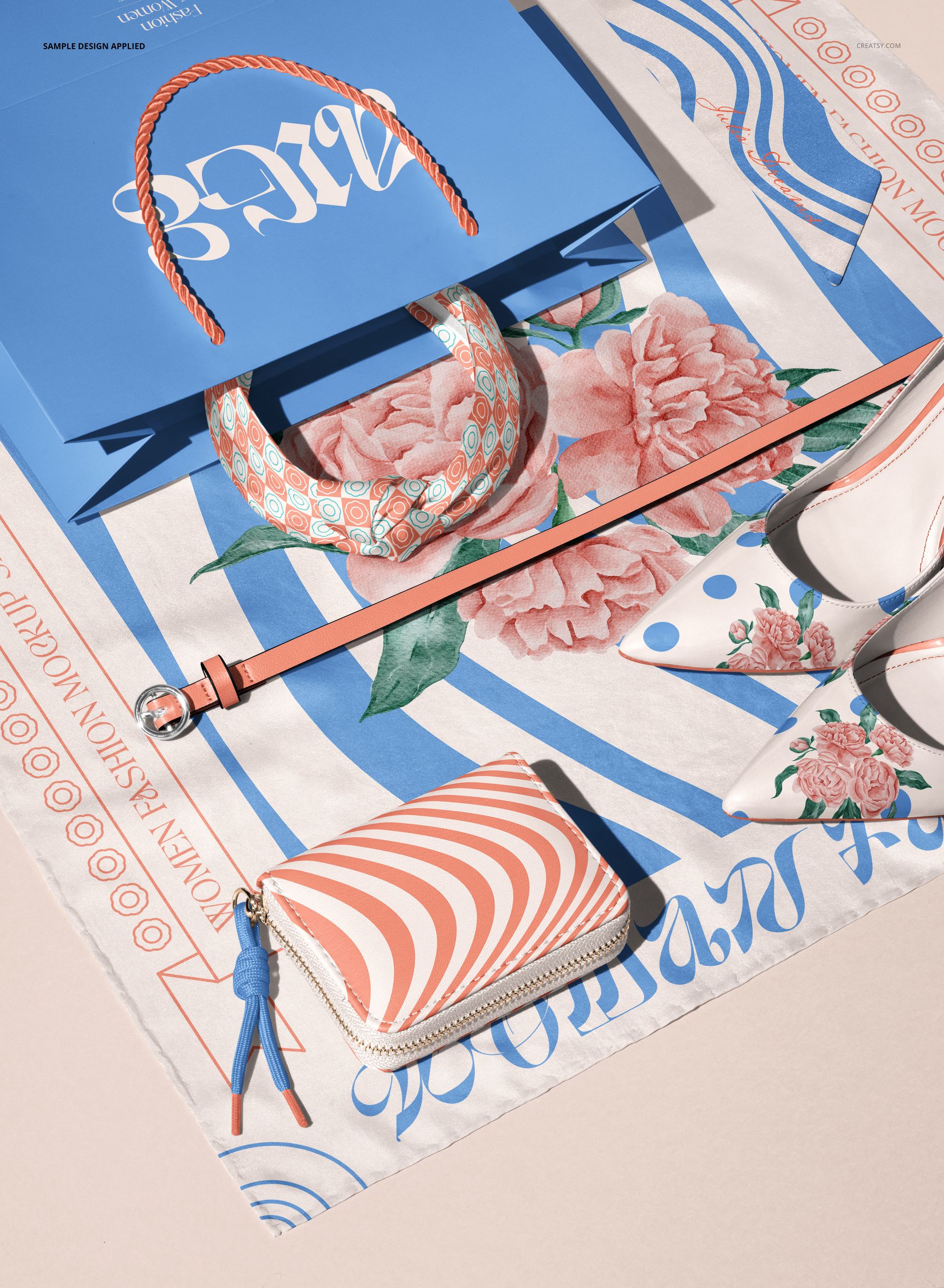 Top view of a mockup scene featuring a blue paper bag, patterned silk scarf, leather belt, wallet, and floral shoes on a printed textile.