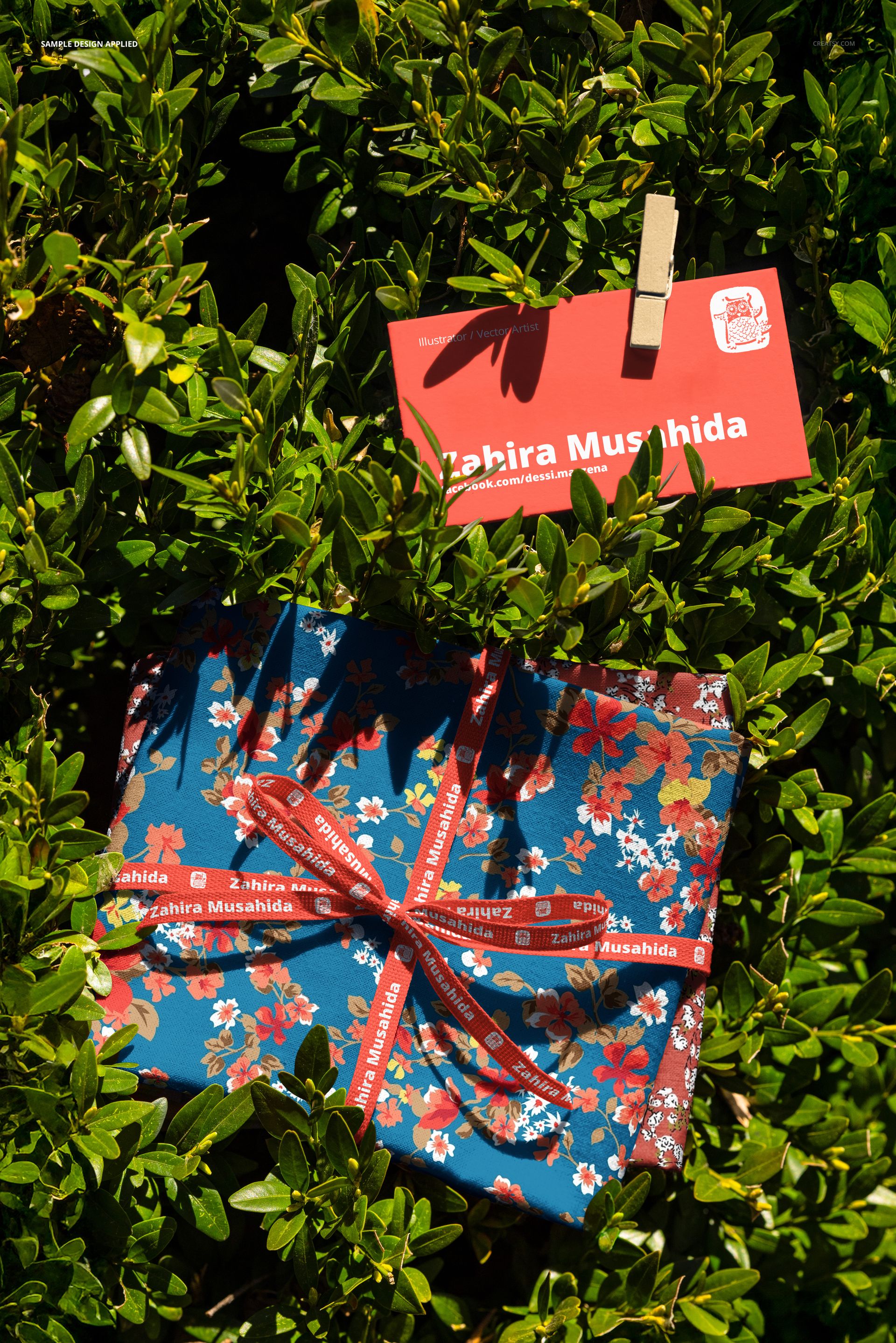 PSD mockup showing colorful floral fabric swatches and a red card clipped to a shrub, viewed from above.