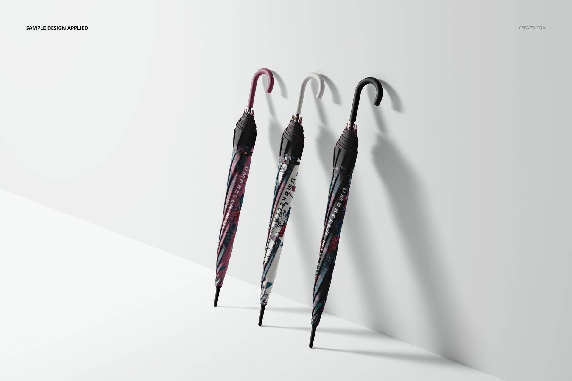 Umbrella mockup featuring trio of closed umbrellas in assorted colors and patterns, leaning against a plain white background.