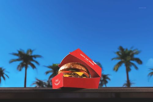 Cheeseburger in a red burger box mockup displayed outdoors with palm trees and blue sky in the background.