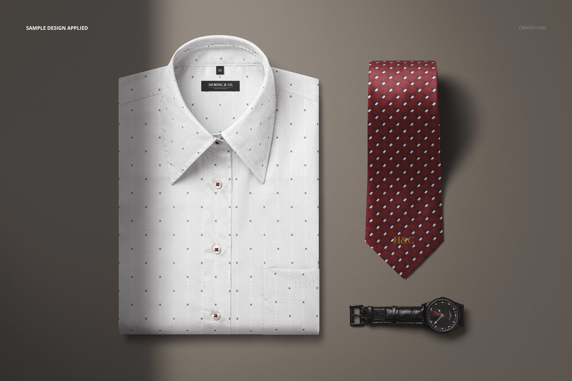 PSD mockup showing a folded white dress shirt, patterned burgundy tie, and black leather strap wristwatch from above on a gray backdrop.