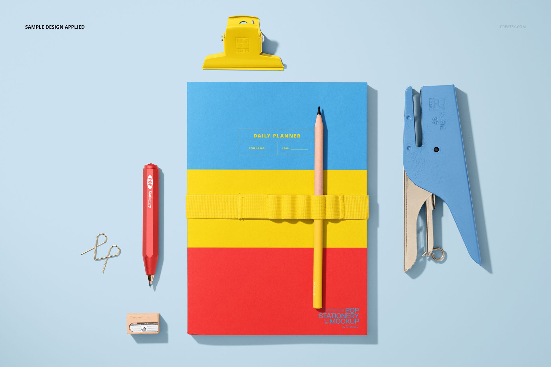 Stationery mockup featuring a notebook with bold horizontal stripes, pencil, stapler, pen, clip, and eraser arranged neatly.