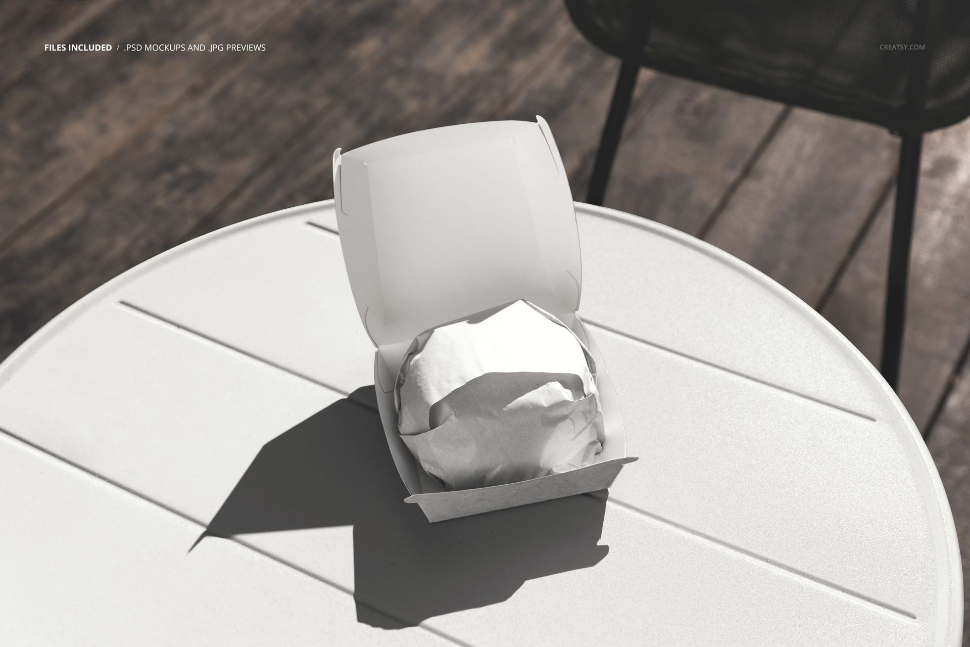 PSD mockup showing a wrapped burger inside a white takeaway box on a sunlit round table in an outdoor setting.