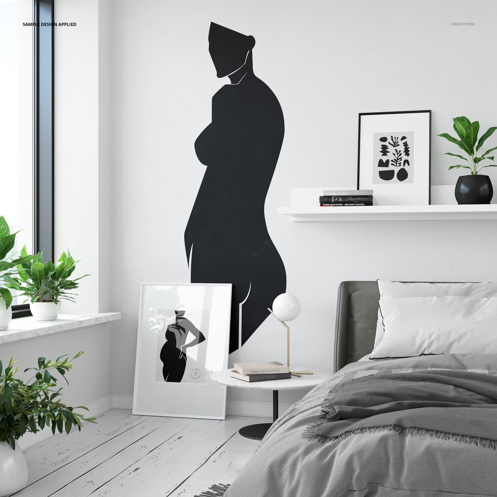 PSD mockup showing a bedroom interior with a bold black wall decal, shelf with art prints, and cozy bed setup.