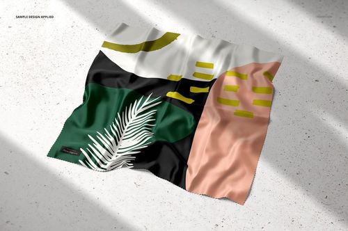 Top view of a silk textile mockup with geometric shapes and a palm leaf design in green, black, and peach tones.