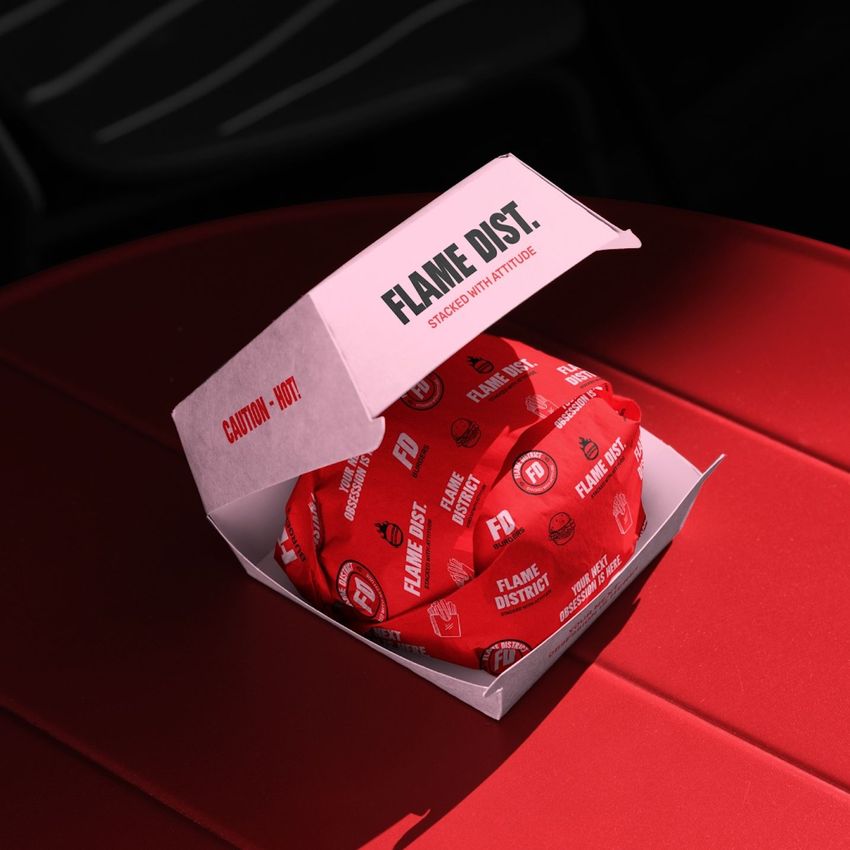Burger box mockup with an open pink container displaying a wrapped burger on a red table, viewed from above in bright lighting.