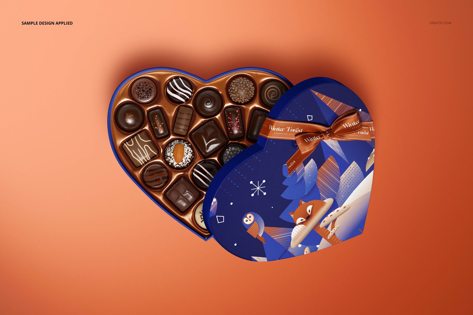 Heart-shaped chocolate box mockup with assorted chocolates inside, blue lid featuring winter-themed illustrations, top view.