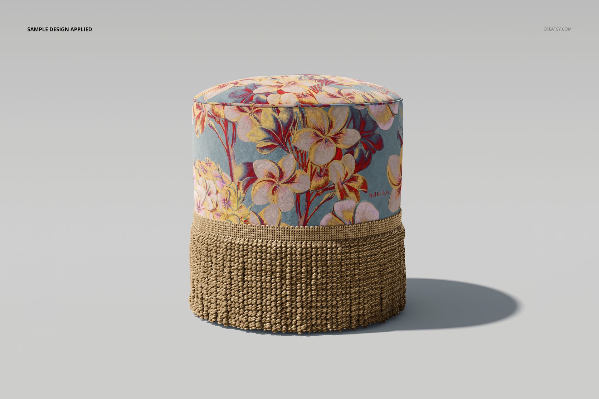 Round velvet footstool mockup with beige fringe, featuring a floral pattern in yellow and pink on a blue background.