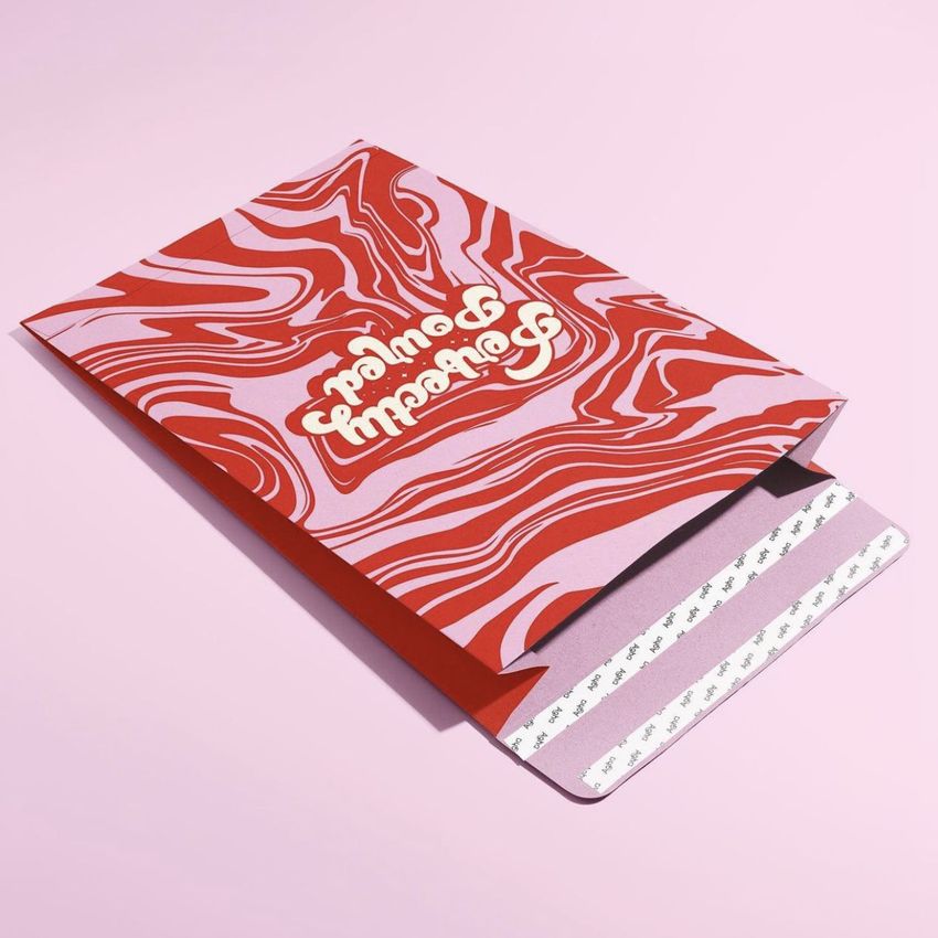 Kraft mailer mockup featuring a red and pink marbled pattern with white text, displayed on a pastel pink background.