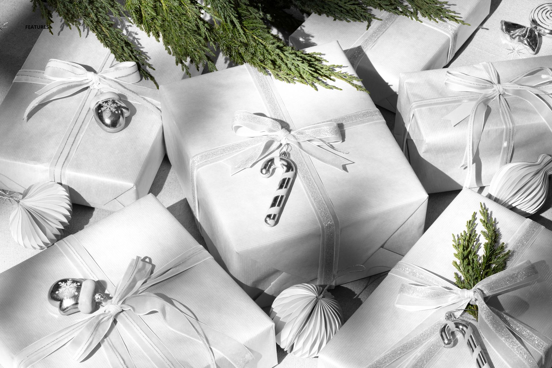 Christmas gift boxes wrapped in white paper with ribbons and festive ornaments, arranged under a tree in a top view mockup.