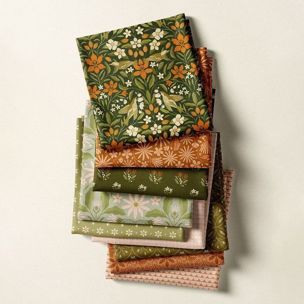 Fabric stack mockup featuring folded textiles with floral and botanical patterns in green, orange, and beige tones on a neutral background.