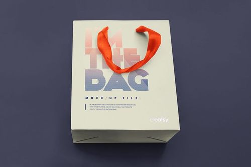 Square gift bag mockup displayed from above, featuring a cream color, dotted text pattern, and bright orange handles.