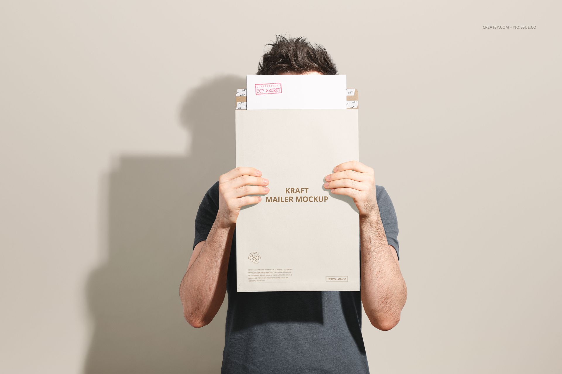 Front view of a person in a dark shirt holding a kraft mailer mockup envelope, obscuring their face from view.