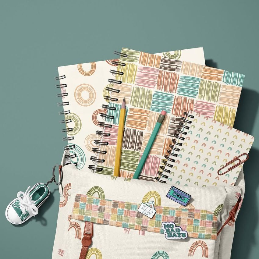 Stationery mockup featuring a school backpack with colorful brush stroke patterns, spiral notebooks, pencils, and a sneaker keychain on a teal background.