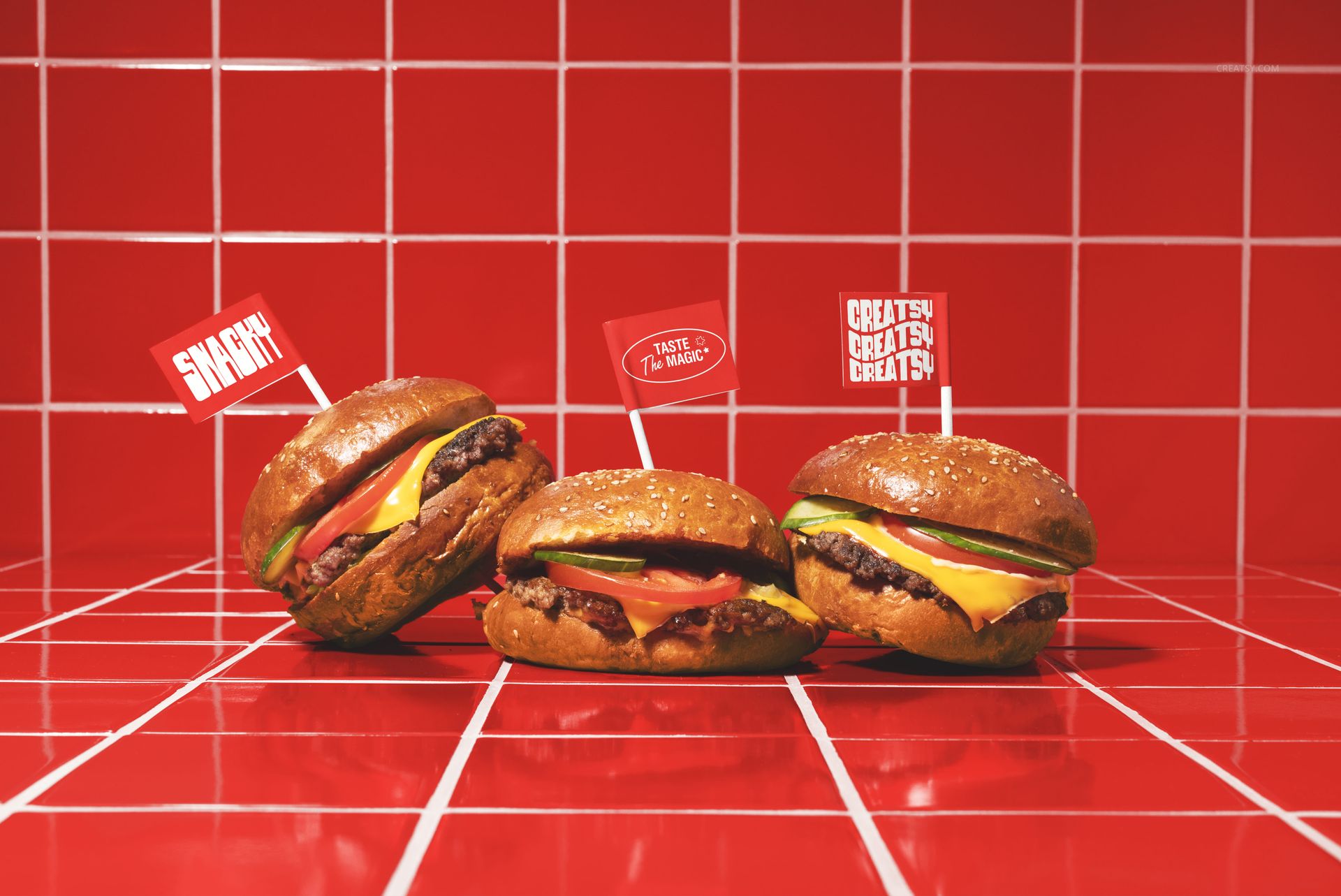 PSD mockup showing three cheeseburgers with toppings and branded flags, arranged on a red tiled countertop.